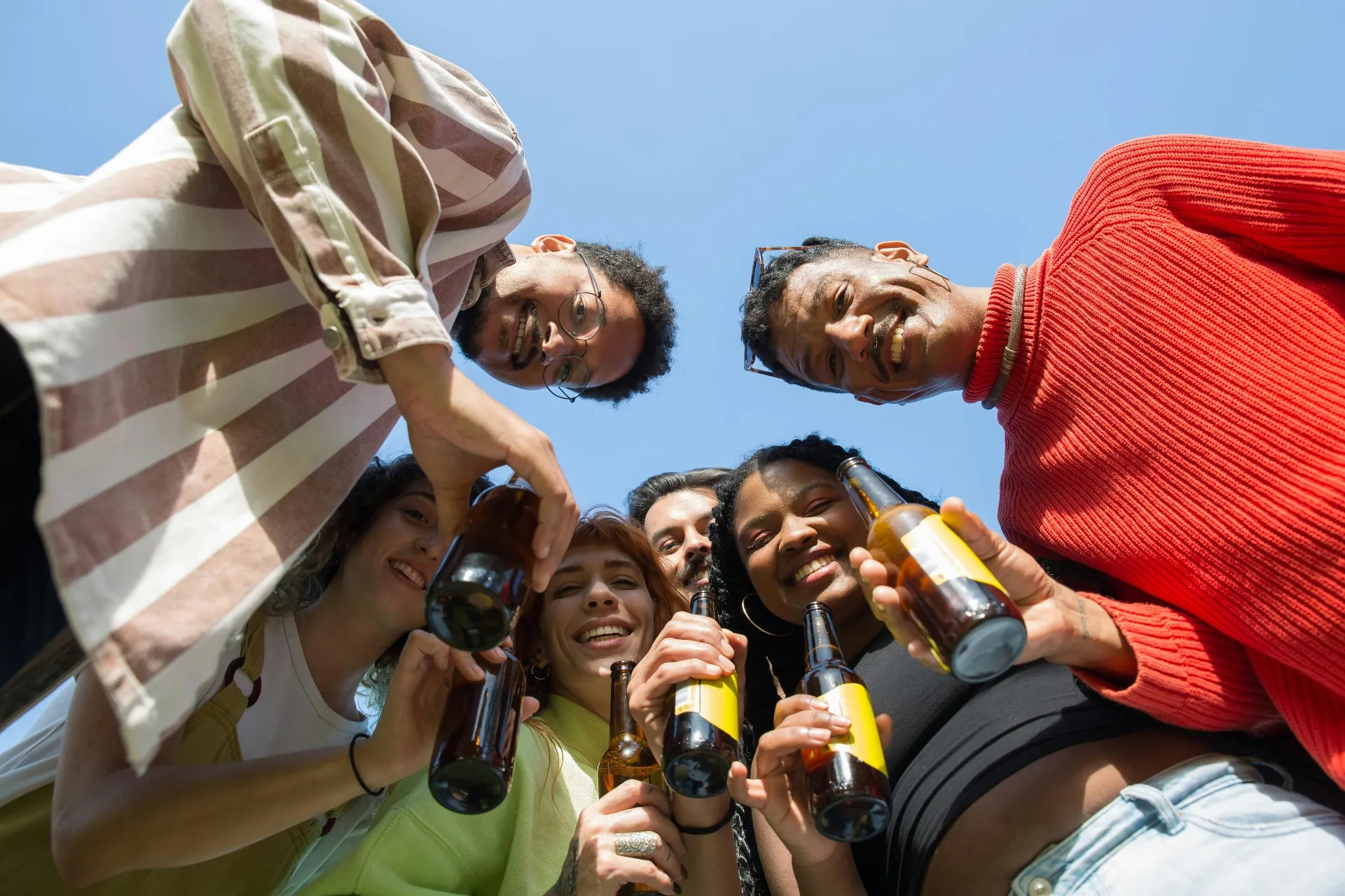 Friends raising bottles together under a clear blue sky